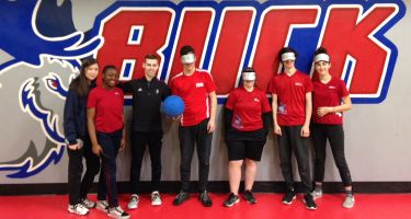 Photo de groupe de l'athlète Simon Richard et six élèves de l'école secondaire Monseigneur-Richard devant le logo de l'équipe sportive scolaire.