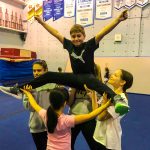 Programme Du sport pour moi! Printemps 2019 - Cheerleading. Capitale-Nationale. Liam en grand écart, les bras en V, supporté par Noémie, Madeleine, Amélie et Vicky.