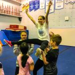 Programme Du sport pour moi! Printemps 2019 - Cheerleading. Capitale-Nationale. Madeleine en grand écart, les bras en V, supporté par Noémie, Liam et Vicky.