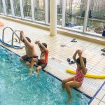 Du sport pour moi! - Natation. Montréal - Printemps 2019. Les enfants sont assis sur le bord de la piscine, les bras joints au-dessus de la tête, pour faire la fusée.