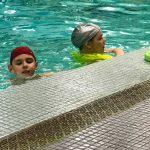 Programme Du sport pour moi! Printemps 2019 - Natation. Capitale-Nationale - Printemps 2019. Lou-Félix et Madeleine dans l'eau, sur le bord de la piscine.
